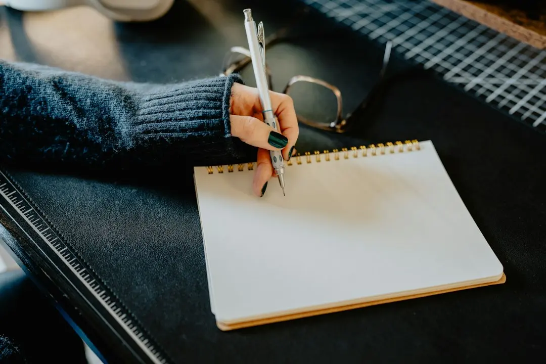 A person writing a checklist in a spiral notebook, comparing IPTV services before choosing one