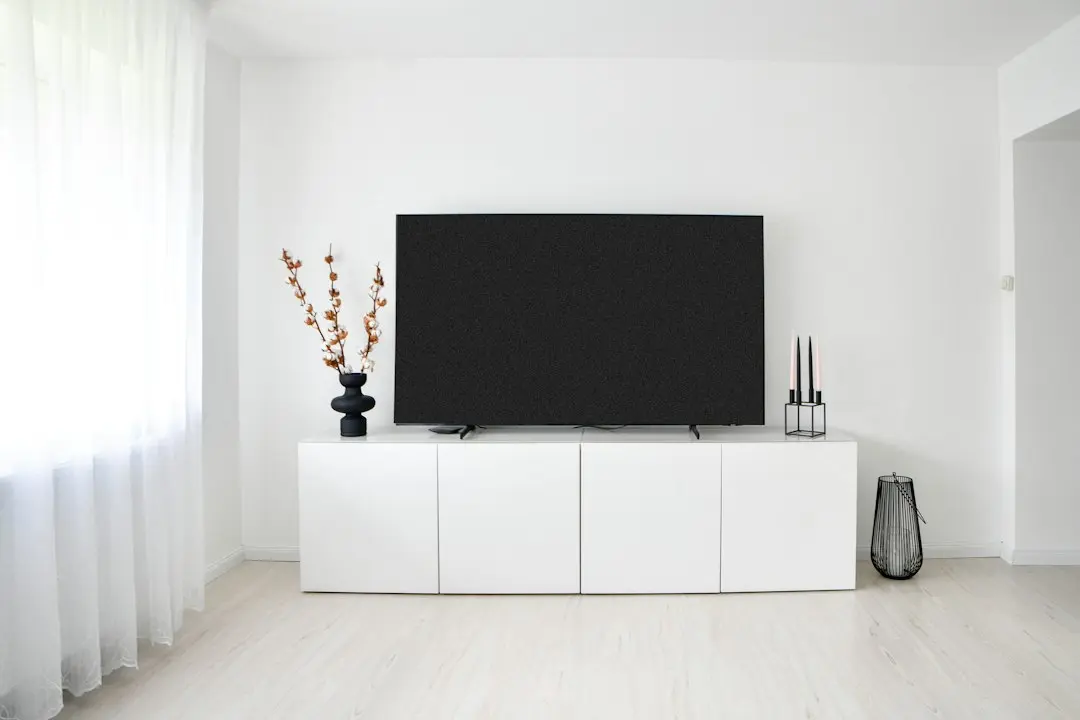 A large TV switched off on a white cabinet in a minimal living room, ready for a Fire TV Stick in its HDMI port