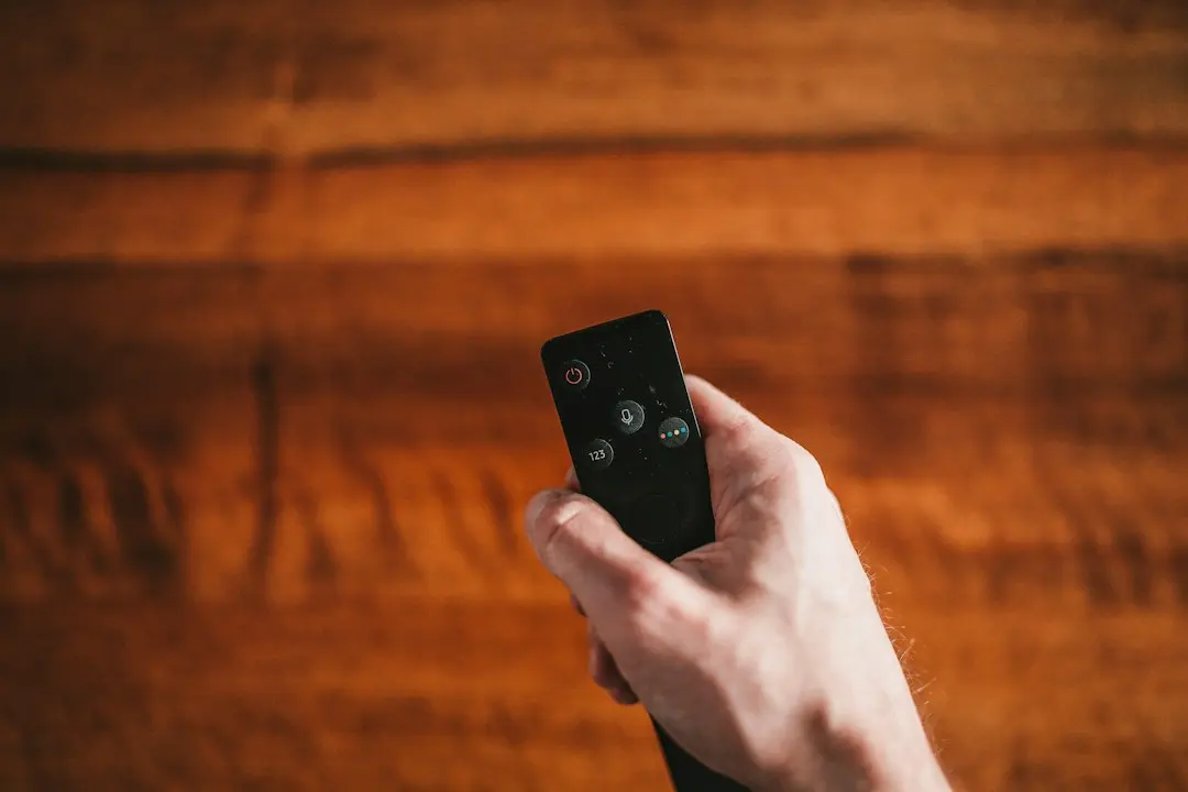 A hand holding a TV remote control against a wooden background, ready to open IPTV Smarters Pro